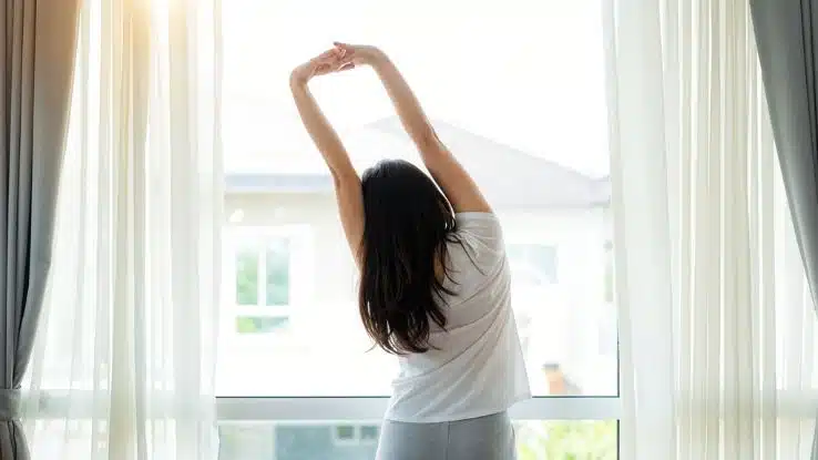 mujer realizando estiramientos suaves de brazos y espalda en un salón luminoso
