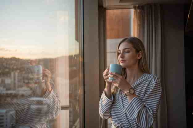 una mujer disfrutando de una taza de té mientras mira por la ventana a la luz del amanecer